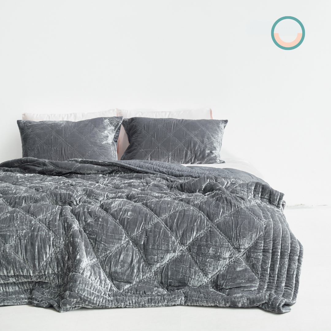 A bed with a grey silk velvet comforter and pillows.
