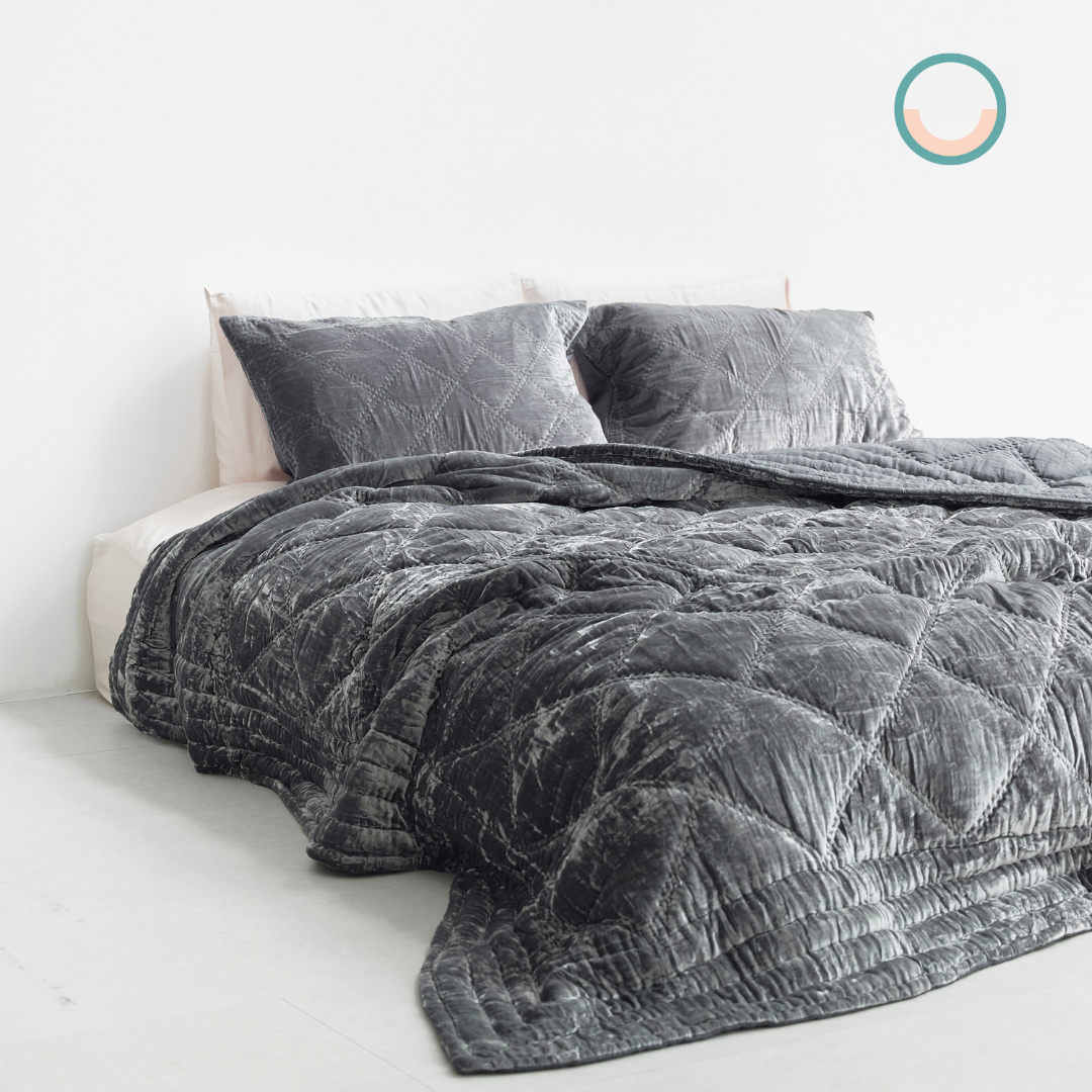 A bed with a grey silk velvet comforter and pillows.